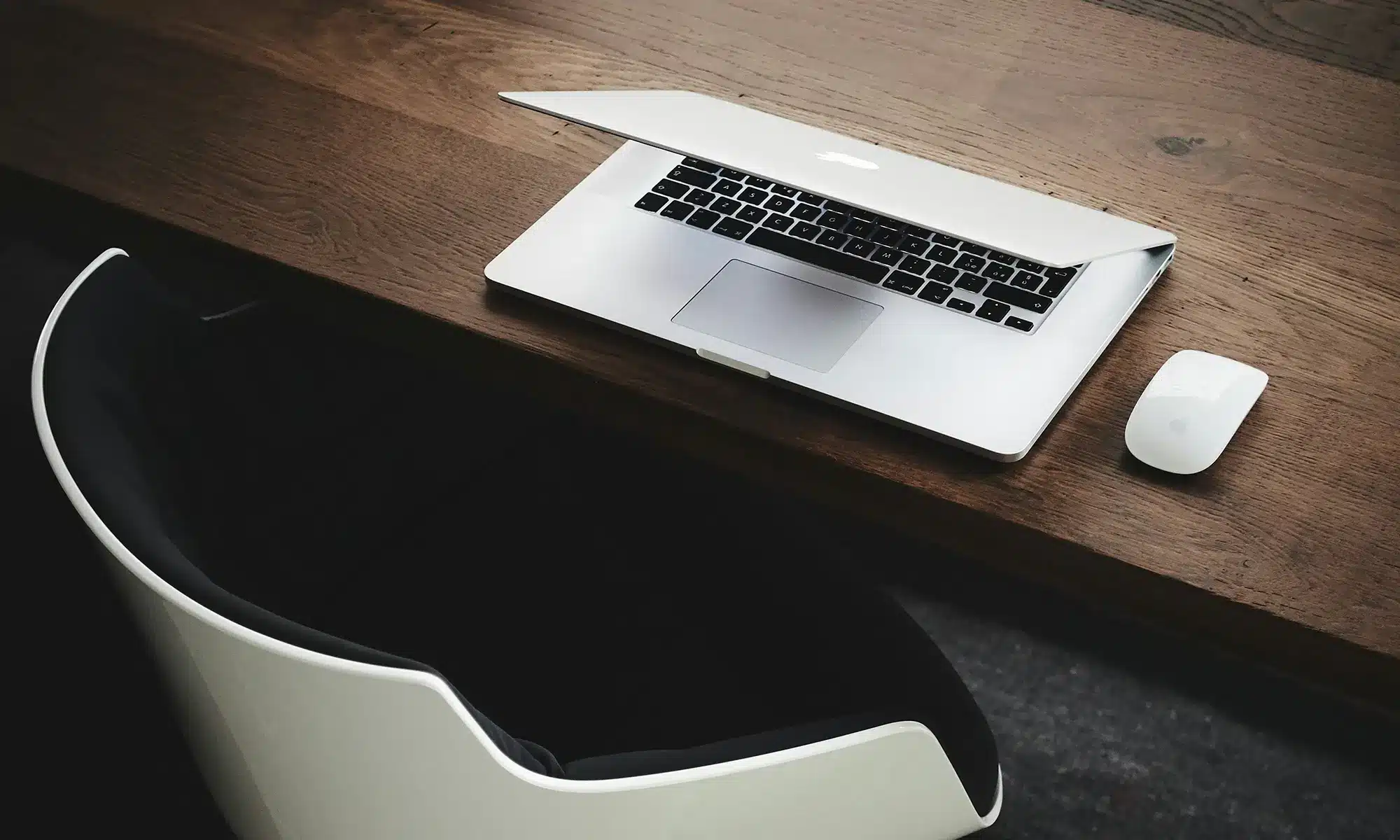 Bureau en bois avec ordinateur portable fermé, souris Apple blanche et chaise design, ambiance de travail professionnelle et chaleureuse.